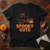 Black t-shirt with orange text "Spooky Cute" and an orange illustration of a cat in a witch hat riding a