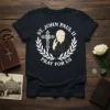 Black t-shirt with "St. John Paul II Pray For Us" text, portrait of the Pope, and a cross within a