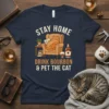 Stay Home Drink Bourbon & Pet The Cat quote with a relaxed cat reading in a chair and bourbon bottle