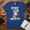 Stay Nutty t-shirt design with a cartoon squirrel wearing sunglasses, holding a coffee cup, and sitting on books