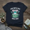 T-shirt design with "Stay Safe & Cosy Koala Hugs" text, featuring a cute koala wearing a mask in a teacup