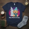 Stay Warm & Cozy t-shirt design with a golden retriever wearing a hat and scarf next to a decorated Christmas