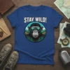 Stay Wild! text above a monkey wearing sunglasses reflecting mountains, on a blue t-shirt design
