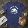 Stay At Home Cat Mom text with a sleeping cat on books and paw prints, white design on navy t-shirt