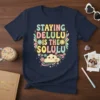 Staying Delulu Is The Solulu quote in colorful retro font with flowers and a cloud graphic on a navy t-shirt