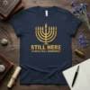 Hanukkah t-shirt with gold text "Still Here Always Will Remember" and a gold menorah graphic