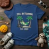 Still In Training Est. 2023 t-shirt with a sloth wearing cycling gear relaxing in a hammock between palm trees