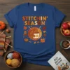 Stitchin' Season text with autumn leaves and a mug of yarn, on a blue t-shirt