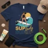 SUP Lady SUPS UP t-shirt featuring a woman paddleboarding on a wave, with bold yellow and blue text