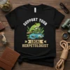 Support Your Local Herpetologist t-shirt with a frog holding a magnifying glass over a blue lizard