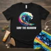 Black t-shirt with "Surf The Rainbow" text and a surfer riding a colorful, stylized wave