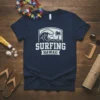 Surfing Hawaii graphic tee featuring a crashing wave, palm tree, and sun, with bold white text