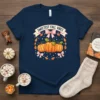 Navy t-shirt with "Sweetest Fall Vibes" text above pumpkins and pink bows, surrounded by autumn leaves
