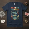 T-shirt with "TABLES TURNED" text and cartoon graphic of overturned tables, chairs, cards, and dice