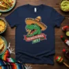 Tacoasaurous Rex T-Shirt featuring a cartoon Tyrannosaurus Rex wearing a sombrero and eating tacos