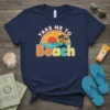 Take Me To The Beach text with sunset, palm trees, and ocean graphic on a navy blue t-shirt