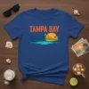 Tampa Bay t-shirt design with orange text, bridge, palm trees, and a sunset over water