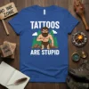 Tatoos Are Stupid t-shirt design featuring a cartoon caveman pointing at himself, with white text and a forest background