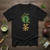 Black t-shirt with "茶 Tea" in Japanese calligraphy and a green matcha whisk symbol surrounded by leaves