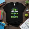 Black t-shirt with "TEACH & ENJOY" text, an open book, a smiling sun, and musical notes graphic