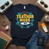 Teacher Mode Off text design with tropical palms, surfboard, and sunset graphic on a navy t-shirt