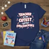 Navy t-shirt with bold white and red text reading "TEACHER OF THE CUTEST LITTLE FIRECRACKERS," surrounded by fireworks graphics