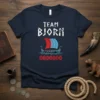 Team Bjorn text above a Viking longship with red and blue sails and rune symbols below, on a navy t-shirt