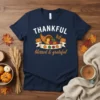 Navy blue t-shirt with "THANKFUL blessed & grateful" text and a harvest cornucopia graphic featuring pumpkins, apples, and wheat
