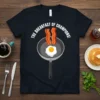 THE BREAKFAST OF CHAMPIONS! text above a frying pan with egg and bacon on a black t-shirt
