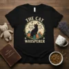 The Cat Whisperer t-shirt design featuring a black cat surrounded by kittens, birds, and musical notes within a wreath