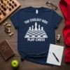 Navy blue t-shirt with white text "The Coolest Kids Play Chess" above a chessboard graphic, designed for young chess players