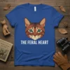 Blue t-shirt with "THE FERAL HEART" text and a stylized brown cat face graphic, featuring green eyes and striped markings