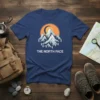 The North Face mountain graphic t-shirt featuring a snow-capped peak, crescent moon, and pine trees under an orange sky