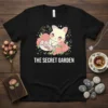 The Secret Garden t-shirt design with a white cat sleeping among pink roses and green leaves, with sparkling stars