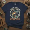T-shirt with text "THERE'S ALWAYS A BETTER CATCH" featuring a jumping fish graphic, fishing lure, and rope circle