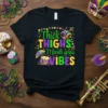Thick THIGHS Mardi Gras VIBES text design with Mardi Gras mask, drum, and beads on a black t-shirt