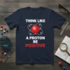 Navy blue t-shirt with white text "THINK LIKE A PROTON BE POSITIVE" and a red atom graphic