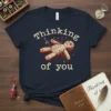 Navy t-shirt with "Thinking of You" text and a voodoo doll graphic pinned with needles