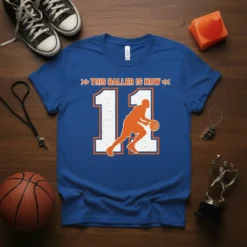 Blue t-shirt with orange and white text "THIS BALLER IS NOW" and a basketball player silhouette dribbling number 11