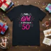 Black t-shirt with "THIS Girl IS OFFICIALLY 50" text in pink and white, surrounded by colorful confetti and fireworks graphics
