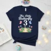 This Little Butterfly 3 is 3 design on a navy blue t-shirt, featuring white text, butterflies, and flowers with the
