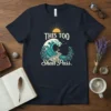 This Too Shall Pass quote on a navy t-shirt with a large ocean wave, stone path, and sun graphic