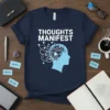 Navy blue t-shirt with white text "THOUGHTS MANIFEST" and a light blue profile head graphic showing neural connections and geometric