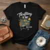 Black t-shirt with white text "Thrifting IS MY therapy" and a shopping cart filled with books and clothing