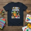 TINY HANDS BIG MESS text with a cartoon dinosaur holding paintbrushes on a navy t-shirt