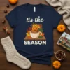 Tis The Season t-shirt with pumpkins, a fireplace, and a cup of warm cider, featuring fall leaves and autumn colors