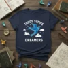 Todos Somos Dreamers t-shirt with a blue origami bird flying among clouds and stars, in white text