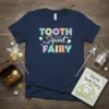 Navy t-shirt with "Tooth Squad Fairy" text in colorful, playful lettering, featuring small tooth graphics and stars