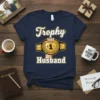 Navy blue t-shirt with "Trophy Husband" text and a wrestling championship belt graphic featuring a gold number 1