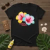 Black t-shirt with "TROPICAL BEAUTY" text and two colorful hibiscus flowers, one yellow and pink, the other blue and pink